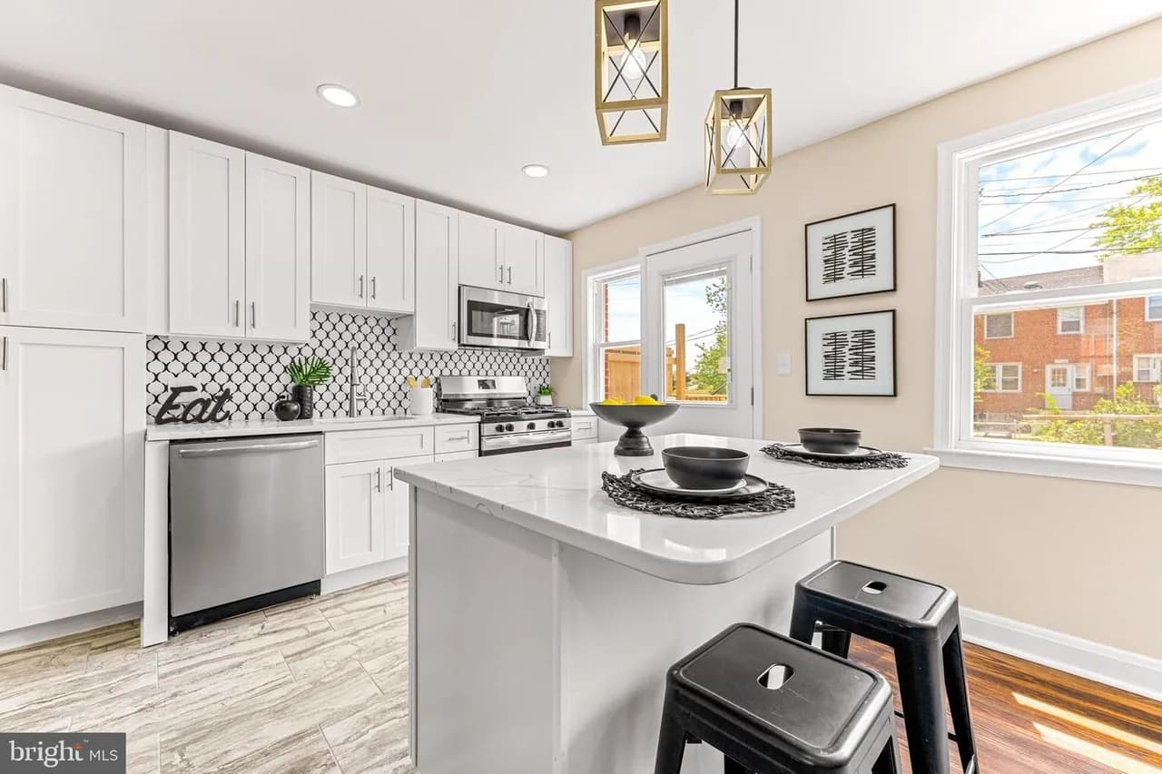 Joan Avenue kitchen with white cabinetry, an island and geometric pendant lights
